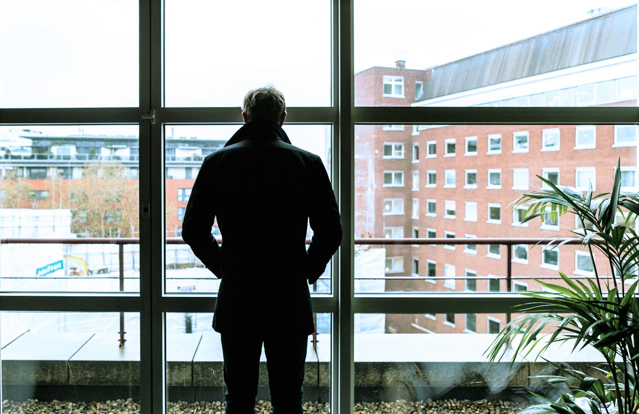 man looking out the window of an office building 