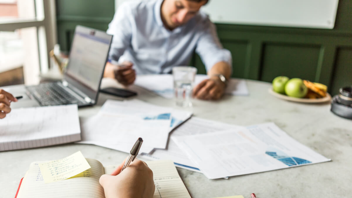 two people working at a table with papers and food